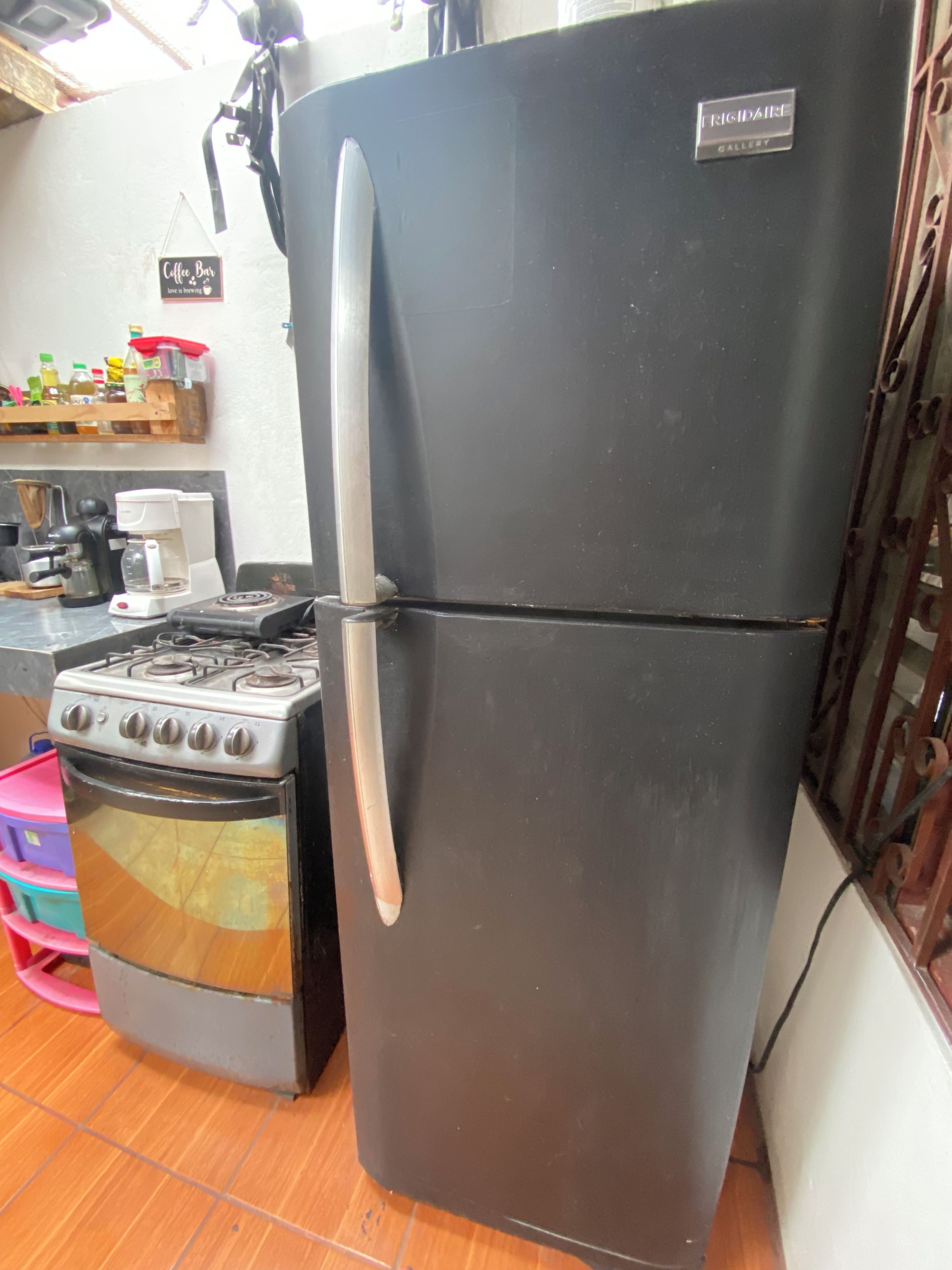 A kitchen with a black refrigerator, a stove, and a coffee maker.