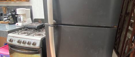 A kitchen with a black refrigerator, a stove, and a coffee maker.