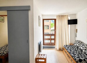A room with a bed, a TV, a small table, and a door leading to a balcony.