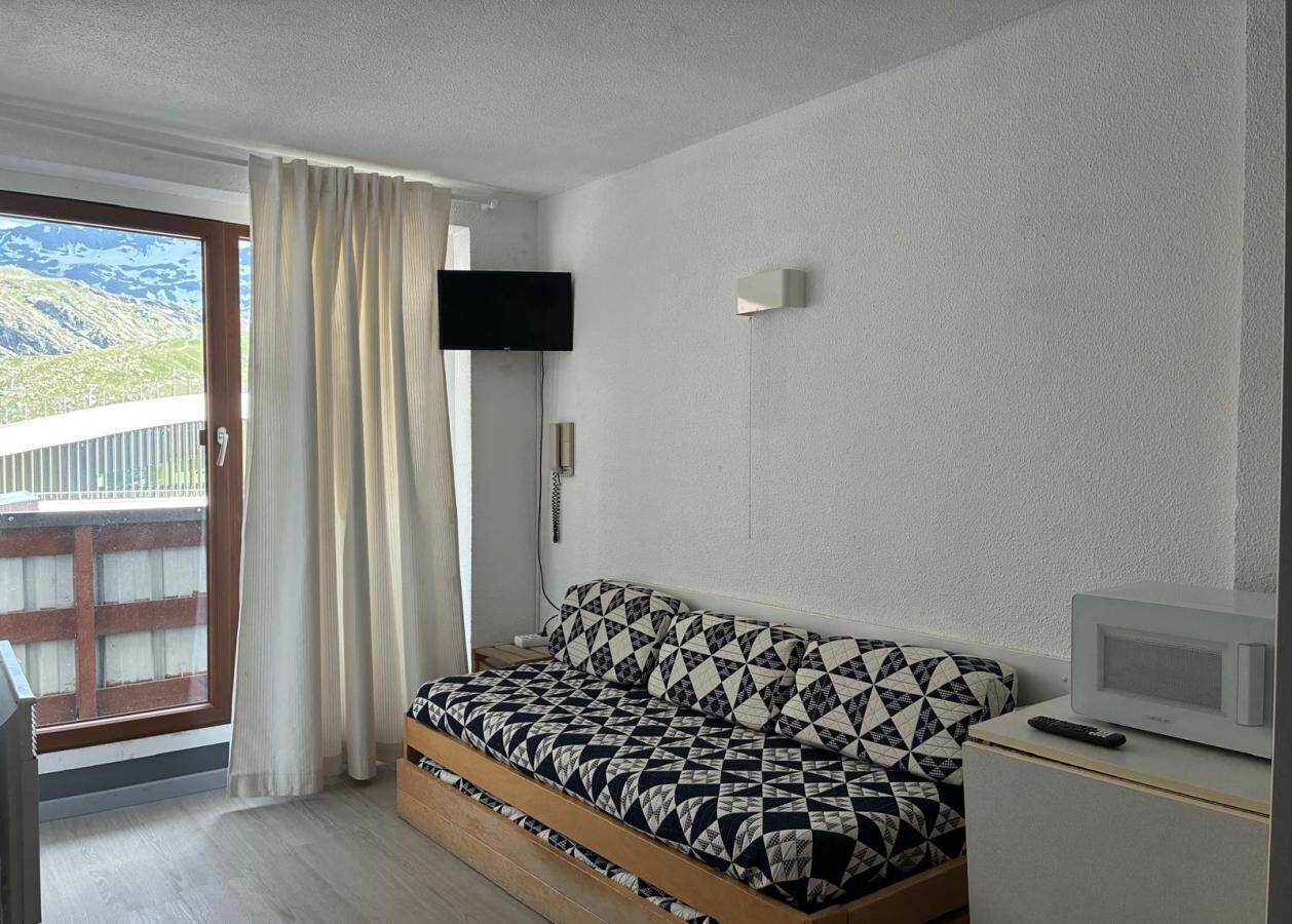 Quarto com cama, televisão, micro-ondas e porta de vidro corrediça para uma varanda.