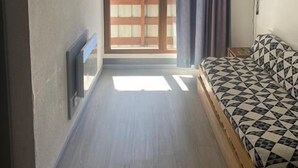 Ein kleiner, gut beleuchteter Raum mit einem Bett, einem an der Wand befestigten Fernseher und einer Schiebetür zu einem Außenbereich.