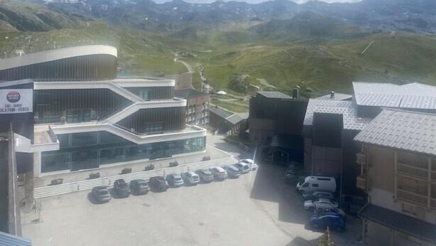 Ein modernes Gebäude mit Parkplatz und einer Berglandschaft im Hintergrund.