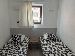 A small room with two beds, a window, and a small table.