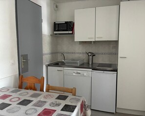 A compact kitchen with a microwave, a sink, and a dishwasher. There is a table with a patterned tablecloth and two chairs.