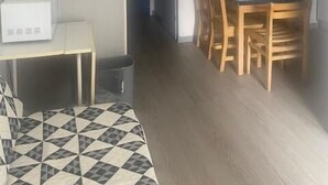 Ein kleiner, gut beleuchteter Raum mit einem Bett, einem Tisch mit einer Mikrowelle, einem Esstisch mit Stühlen und einer Tür, die in einen weiteren Raum führt.