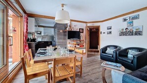 Un vaste espace de vie comprenant une table à manger en bois pour quatre personnes, un canapé en cuir noir et un téléviseur posé sur un meuble en bois.