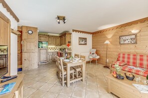 A cozy cabin interior with a dining area, kitchen, and a living room with a sofa and a teddy bear.