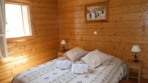 A wooden room with a bed, two bedside lamps, and a window.