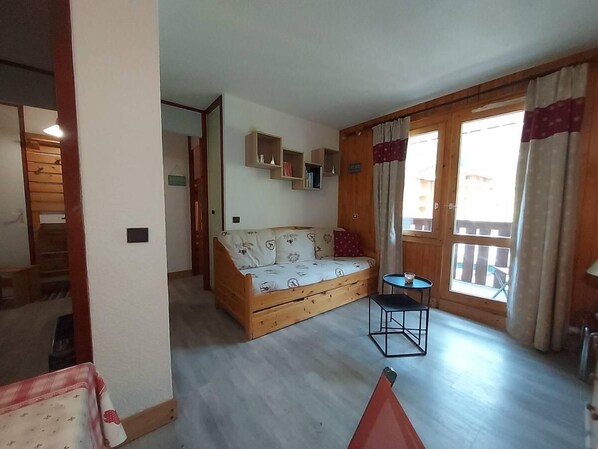 Ein gemütliches Zimmer mit einer Holzsofa, einem kleinen Tisch und einem Fenster mit Vorhängen.