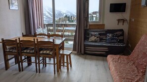 Une pièce comprenant une table et des chaises en bois, un canapé et un téléviseur fixé au mur.