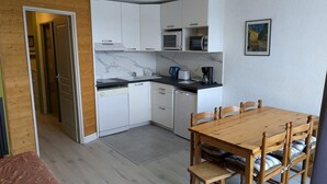 A compact kitchen with white cabinets, a wooden dining table, and a microwave.