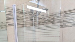 A modern bathroom with a glass shower enclosure, a white bathtub, and a dark-toned vanity with drawers.