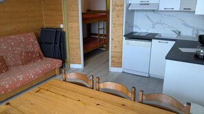Une pièce compacte comprenant un lit superposé en bois, un canapé, une table à manger avec des chaises, un coin cuisine avec un évier et une cuisinière, et un pare-feu en marbre.