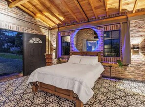Un dormitorio con cama de madera, pared de ladrillo y ventana grande.