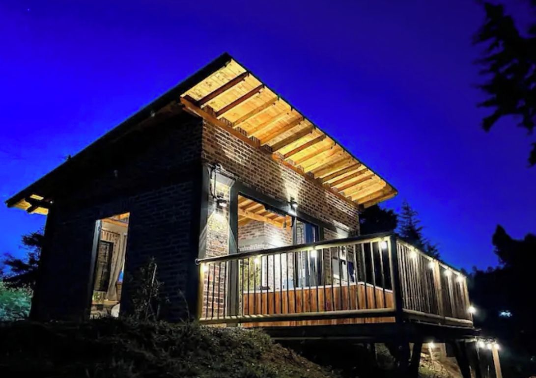 A two-story wooden cabin with a balcony, surrounded by trees.