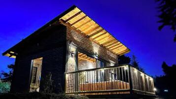 A two-story wooden cabin with a balcony, surrounded by trees.