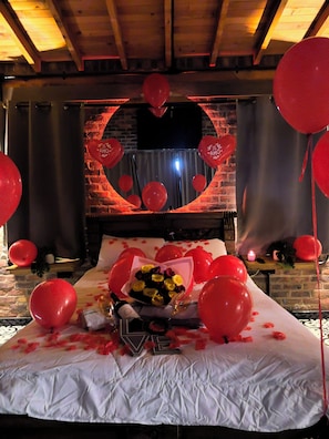 Een bed met een spiegel in de vorm van een hart, rode ballonnen en een boeket gele rozen.