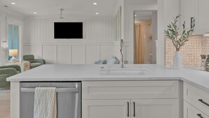 A modern kitchen with a large island, white cabinetry, and a flat-screen TV mounted on the wall.