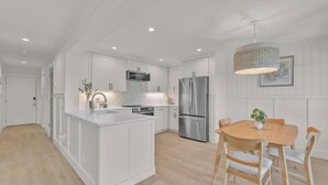 A modern kitchen with white cabinetry, a stainless steel refrigerator, and a wooden dining table with chairs.