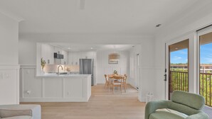 A modern kitchen with white cabinetry, a central island, and a dining area with a wooden table and chairs.