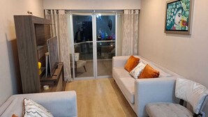 Ein modernes Wohnzimmer mit einer Sofagarnitur, einem Holzkabinett und einer Glastür, die auf einen Balkon mit Stadtblick führt.