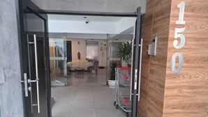 Eine Hotellobby mit Glastür, einer Sitzecke mit Sofa und Sesseln sowie einer Holzwand mit der Nummer 150.