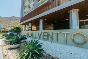 A hotel entrance with the name DELVENTT visible, surrounded by potted plants and a gravel pathway.
