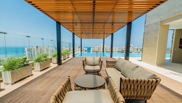 A rooftop terrace with a pool, outdoor seating, and a view of the ocean and buildings.