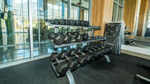 A gym with a rack of dumbbells, large windows, and a view of the outside.