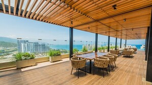 A rooftop terrace with a wooden ceiling, a wooden table, and wicker chairs.
