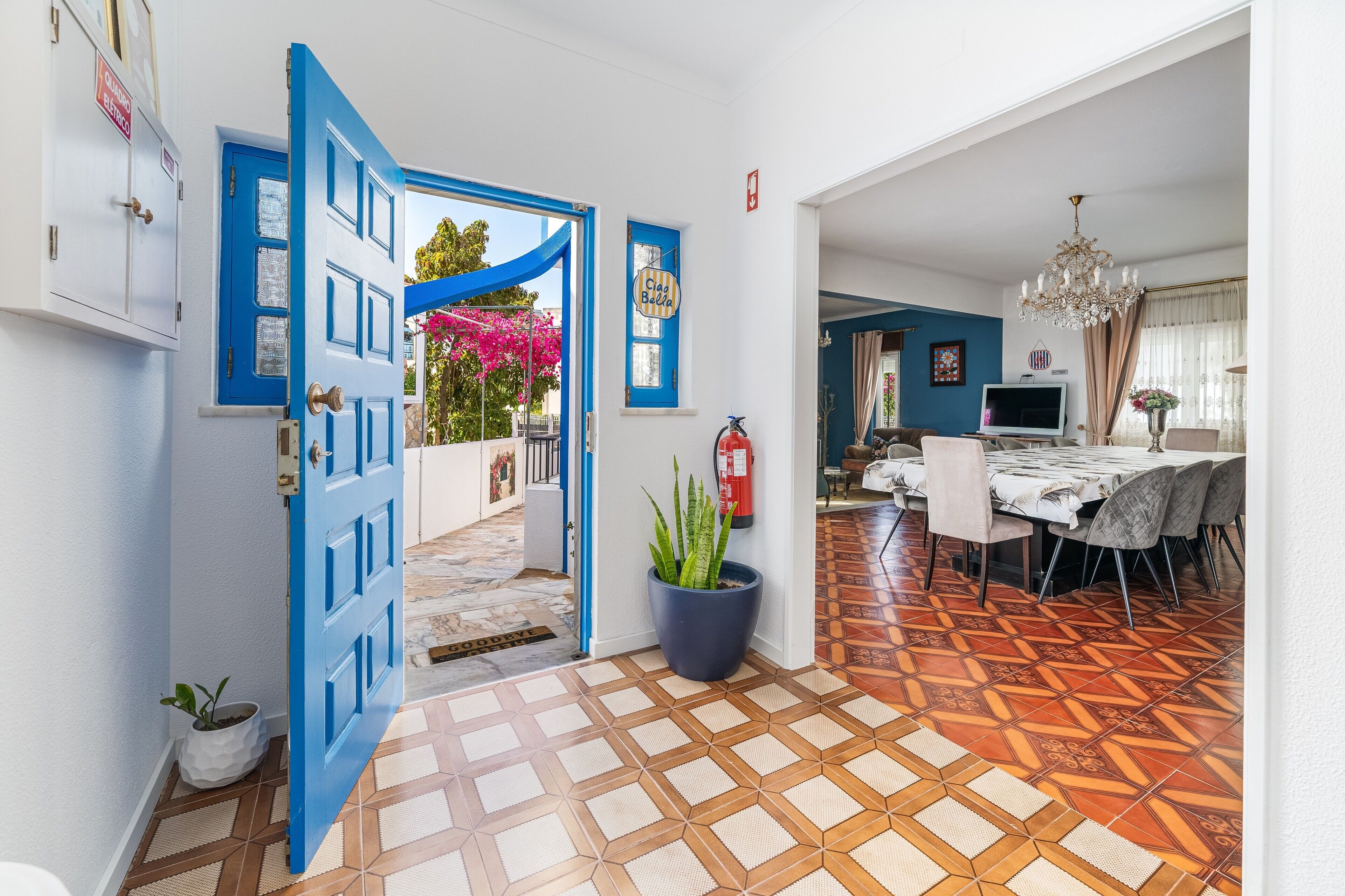 A room with a blue door, a potted plant, a dining area with a table and chairs, and a patterned floor.