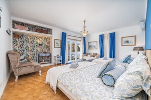 A bedroom with a large bed, a chair, a desk, and a view of the outside.