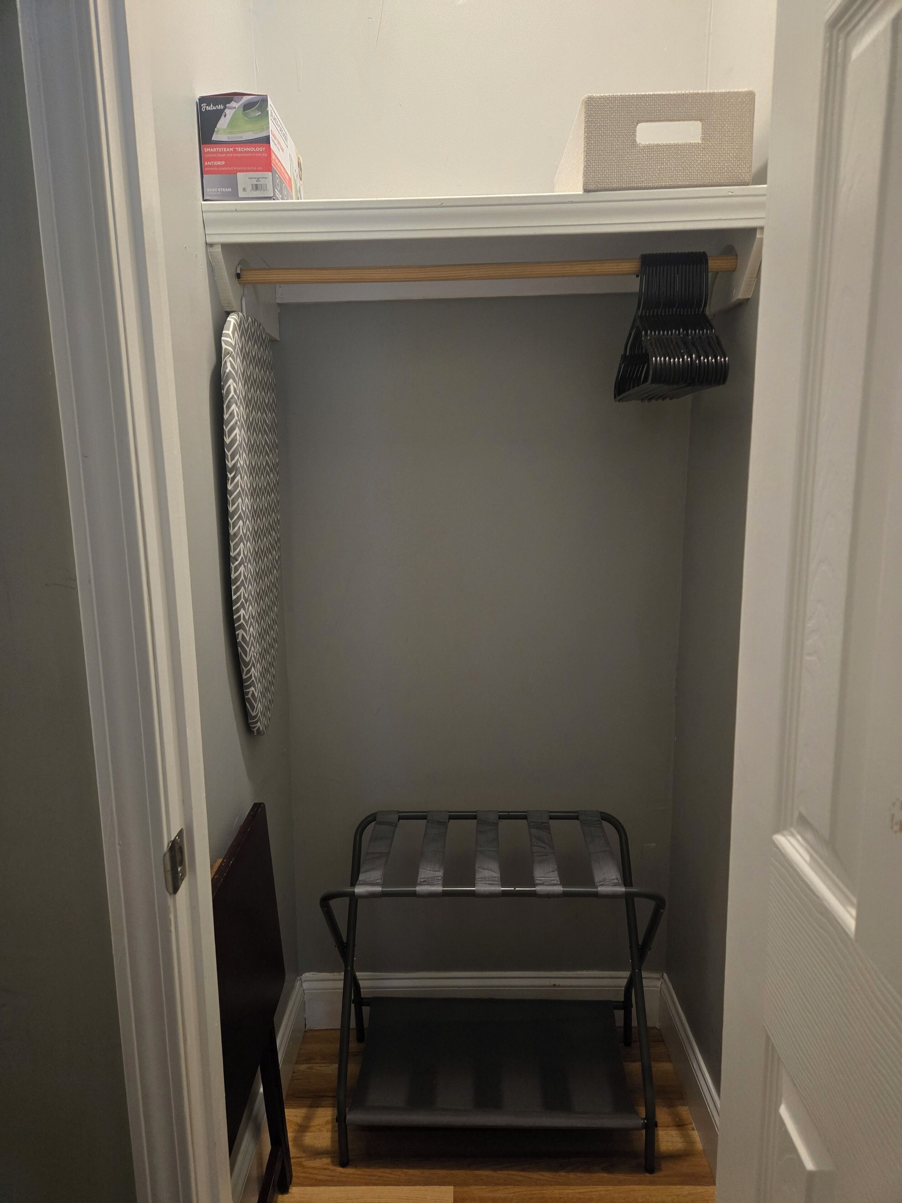 A walk-in closet with a metal shelf unit, a hanging rack, and a storage box on the top shelf.