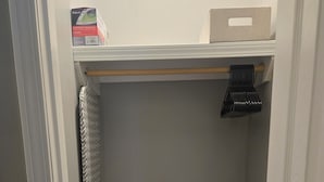 Un vestidor con una estantería metálica, una percha y un contenedor de almacenamiento en el estante superior.