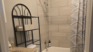 Un baño con inodoro, lavabo, bañera y ducha. Hay un perchero y una botella de jabón de manos sobre la encimera del lavabo.