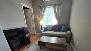 Un espacio habitable compacto con kitchenette, un sofá con cojines, una mesa de centro y una alfombra estampada.