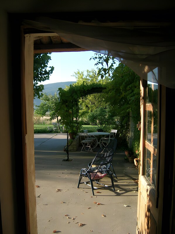 A view through a doorway to a patio area with a table and chairs, a pergola, and a street with a mountain in the background.
