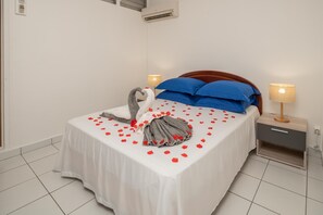 Una cama bien hecha con una colcha blanca, almohadas azules y una figura decorativa de cisne.