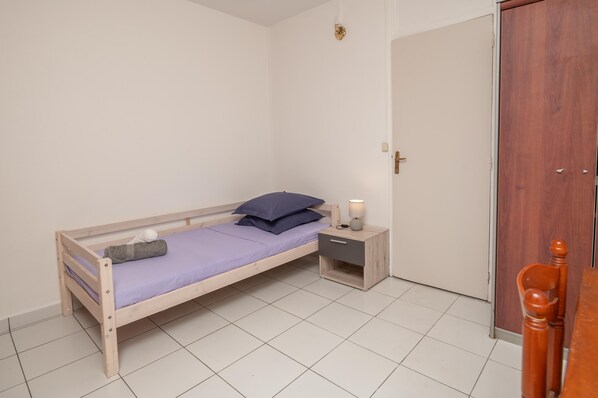 Una habitación pequeña con cama individual, estructura de madera, mesita de noche con lámpara y armario.