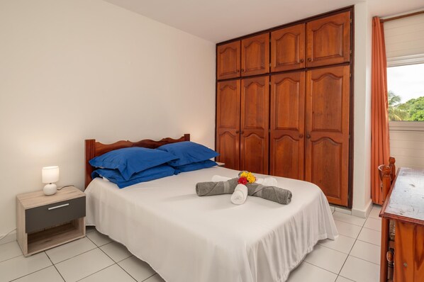 Una cama bien hecha con almohadas azules, un armario de madera y una mesita de noche con una lámpara.