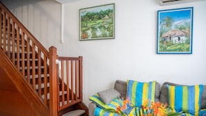 Un escalier avec des rampes en bois, un canapé gris agrémenté de coussins colorés et deux tableaux encadrés accrochés au mur.