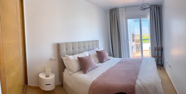 A bedroom with a large bed, a bedside table, and a view of the outdoors through a sliding door.