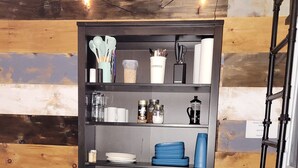 Een keuken met een zwarte wandplank vol keukengerei, een tafel met stoelen, en een zwarte stoel.