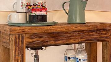 Une table en bois avec une machine à café, une tasse, un pichet et deux bouteilles d’eau.