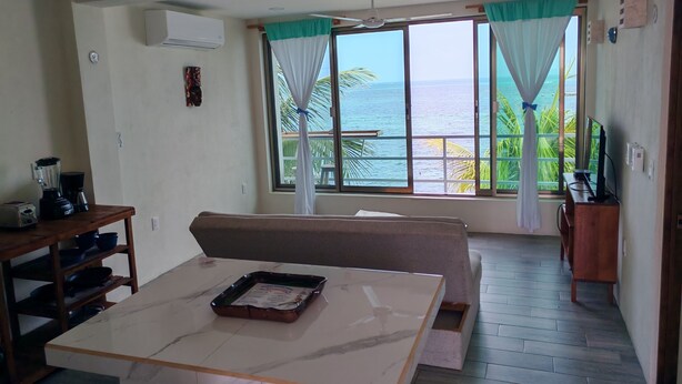 Ein Zimmer mit Esstisch, einer Couch, einem Fernseher und Meerblick.