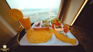 A breakfast tray with a glass of orange juice, a plate of eggs, and various fruits and pastries on a table with a view of the city. - Nile View (Cairo)