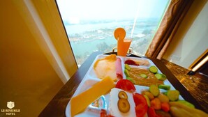 A meal tray with various food items and a drink, placed on a table with a view of a body of water and buildings in the background. - Nile View (Cairo)