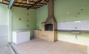 A kitchen with a brick oven, a white refrigerator, and a tiled backsplash. - Casa 4Q em Condomínio c\/ Piscina NAT0202 (Cabo Frio)