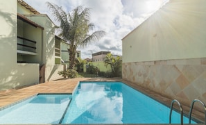 Una piscina con paredes y solárium de baldosas, rodeada de edificios y palmeras.