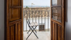 Uma porta de madeira aberta dá para uma varanda com vista para telhas de barro e um corrimão de metal.